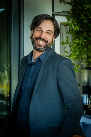 Smiling attendee in a dark blazer by the terrace greenery