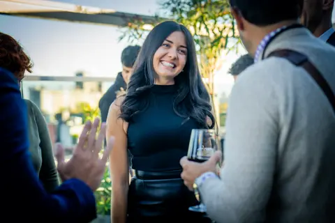 Smiling attendee with a glass of wine in conversation on the rooftop