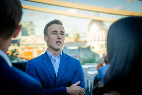 Attendee in a blue blazer listening to another guest, with the Old Montreal skyline behind him