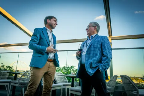 Two attendees talking at the terrace railing at sunset