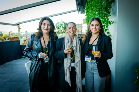 Three attendees posing together with drinks on the rooftop