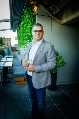 Attendee in a light blazer holding a drink on the terrace