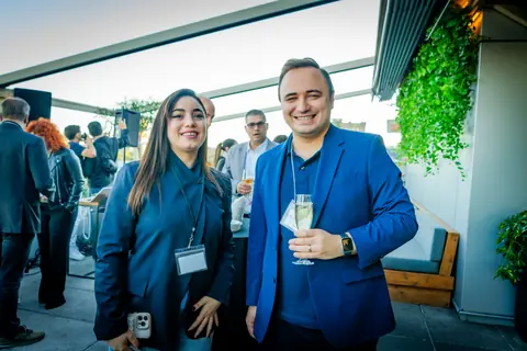 Two attendees smiling with drinks as the rooftop fills with guests