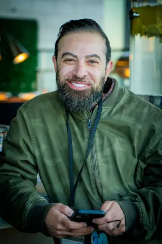 Smiling attendee in a green jacket holding his phone at the rooftop event
