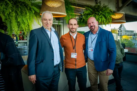 Three attendees with event lanyards posing together by the rooftop bar