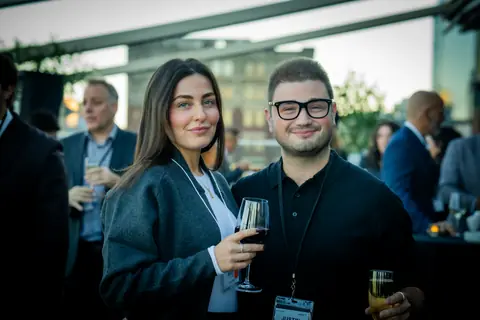 Two attendees smiling with drinks on the crowded terrace