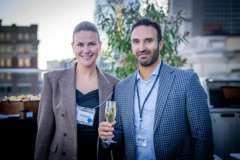 Two attendees with event badges posing together with champagne on the rooftop