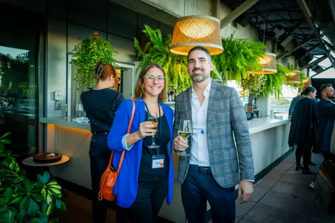 Two attendees with drinks talking under the terrace's woven pendant lights