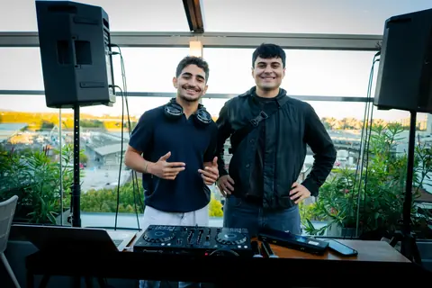 DJ and a guest posing behind the decks with Montreal's Old Port behind them