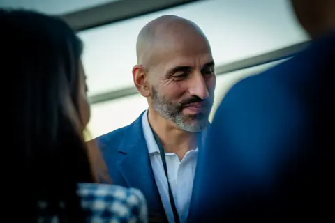 Attendee in a blue blazer smiling during a conversation on the rooftop