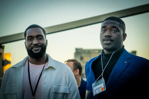 Two attendees with event lanyards on the rooftop at sunset