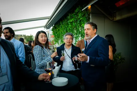 Group of attendees in conversation around a high table under the ivy wall