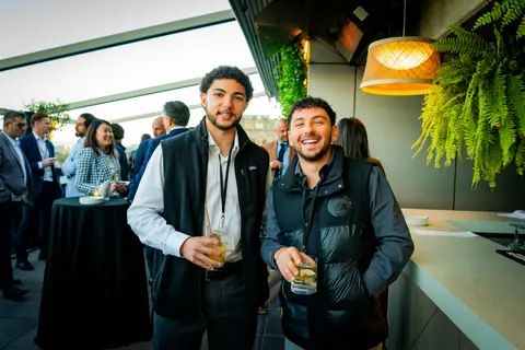 Two attendees smiling with drinks near the rooftop bar