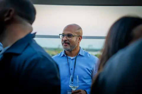 Attendee in a blue shirt with a glass of white wine at dusk