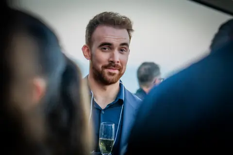 Smiling attendee holding a glass of champagne as evening falls