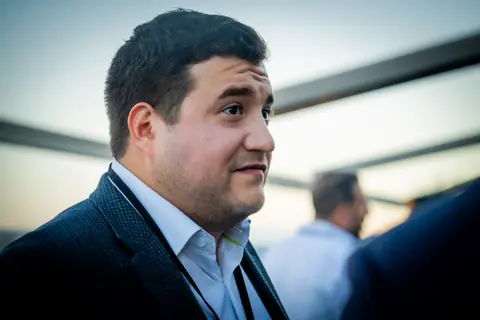 Attendee in a dark blazer speaking with other guests at dusk