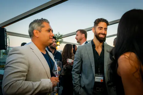 Attendees in blazers talking with drinks on the rooftop