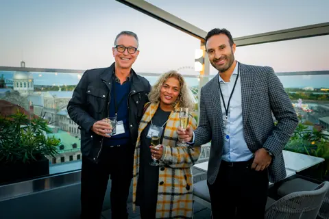 Three attendees posing with drinks with Old Montreal behind them