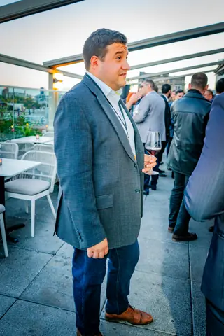 Attendee in a gray blazer standing on the rooftop terrace as guests mingle