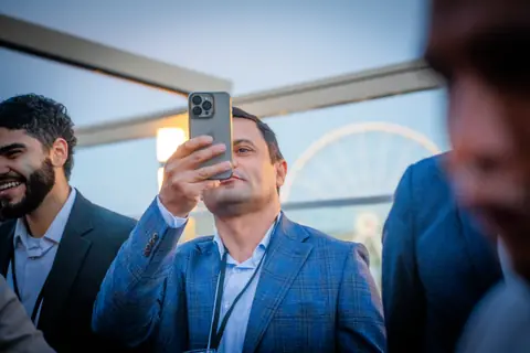 Attendee taking a photo with his phone in front of the Old Port Ferris wheel
