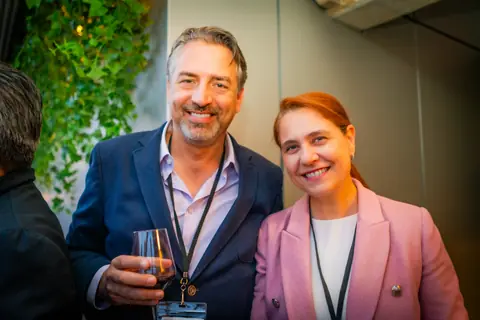 Two attendees smiling together with drinks under the greenery