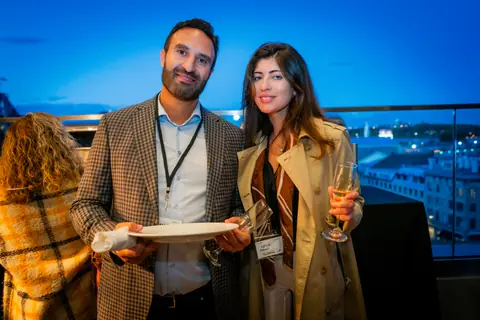 Two guests with event badges smiling on the terrace after sunset