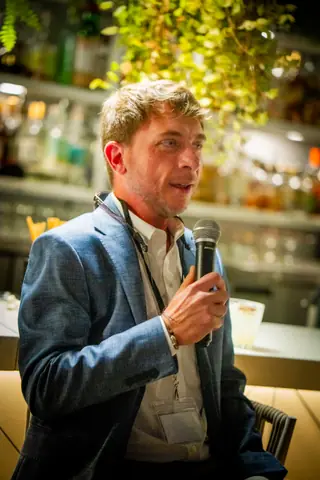 Panelist in a gray blazer answering a question into the microphone