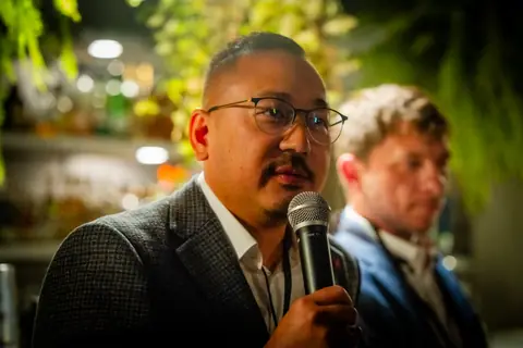 Panelist in glasses answering a question by the bar