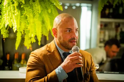 Panelist in a tan blazer making a point into the microphone