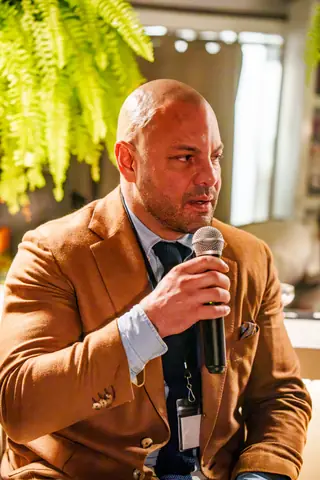 Panelist in a tan blazer speaking from his stool