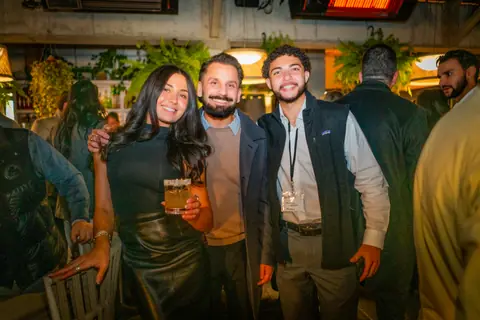 Three attendees smiling together with drinks late in the evening