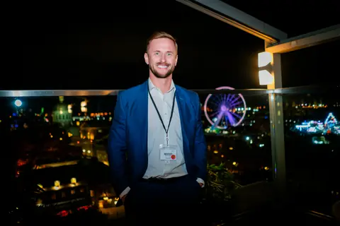 Attendee in a blue blazer with the Old Port Ferris wheel lit up behind him