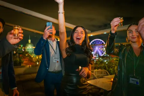 Attendees raising their drinks with Old Montreal and the Ferris wheel lit up at night