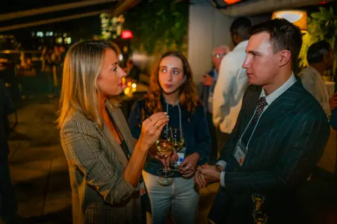 Attendees in conversation along the rooftop railing after dark