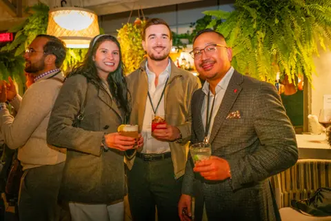 Three attendees with cocktails posing under the pendant lights
