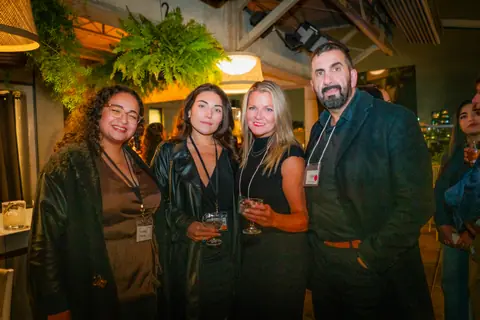 Four attendees with event lanyards posing together under the hanging ferns