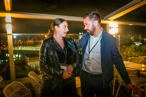 Two attendees talking at the railing with the Old Port lit up at night
