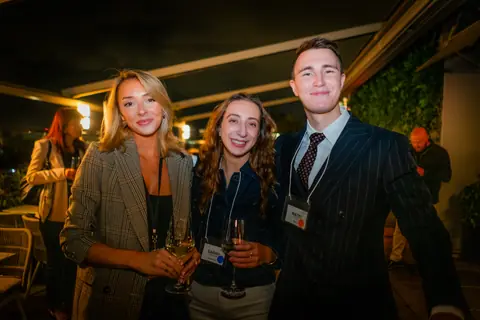 Three attendees with drinks smiling on the terrace at night