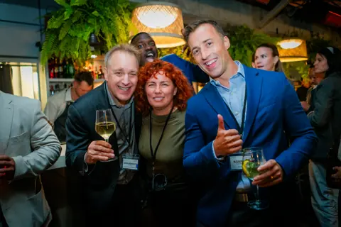 Attendees posing with drinks and a thumbs up near the bar
