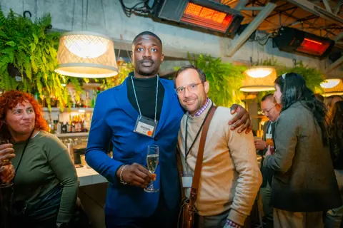 Two attendees with event lanyards posing arm in arm by the bar