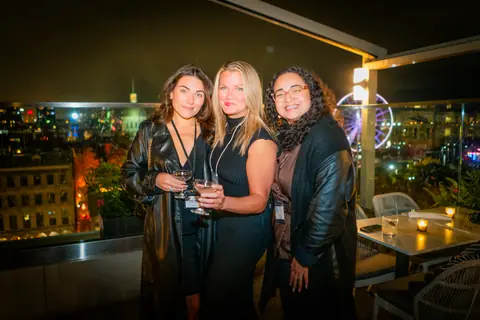 Three attendees posing together with the Old Port Ferris wheel lit up behind them
