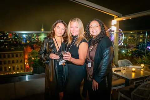 Three guests smiling together on the rooftop late in the evening