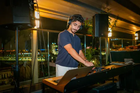 DJ mixing at the rooftop booth with the lights of the Old Port behind him