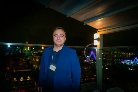 Attendee in a blue blazer with the illuminated Old Port Ferris wheel behind him