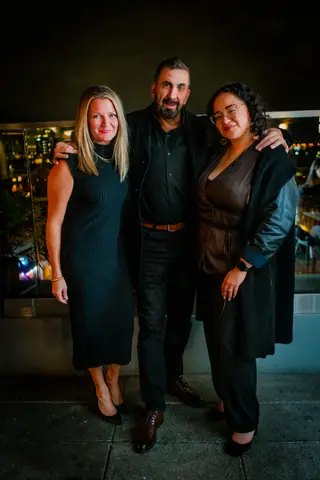 Three attendees posing together on the rooftop at night