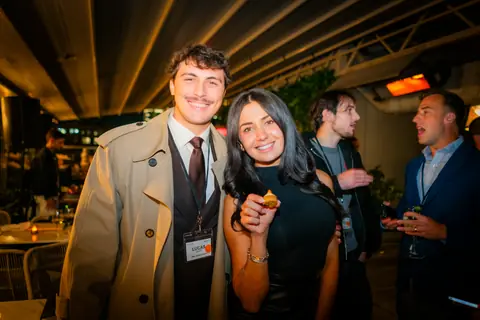 Two attendees smiling with canapés on the rooftop