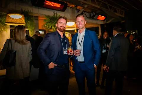 Two attendees with event lanyards posing together with drinks