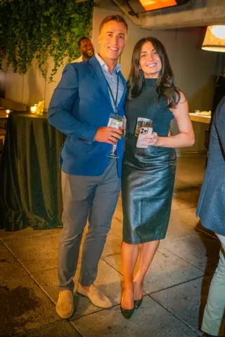Two attendees posing together with drinks by the bar